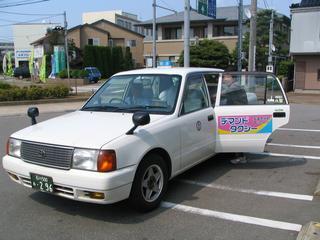 ホワイトカラーの小型タクシー車両に乗り込もうとしている人の写真