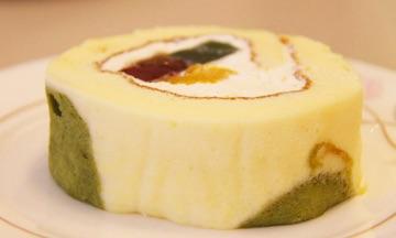 お皿の上に、茶色、緑色、オレンジ色の食材をクリームで包んだロールケーキが置かれている写真