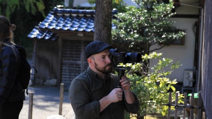 建物の側でカメラを構えて撮影をしている男性の写真