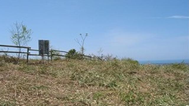 草の生い茂る丘に、柵と看板が立っている写真