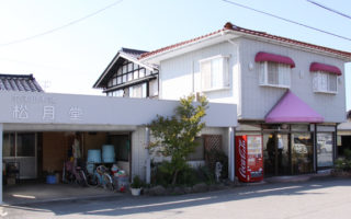 白い外壁にピンクの屋根がある松月堂の外観の写真