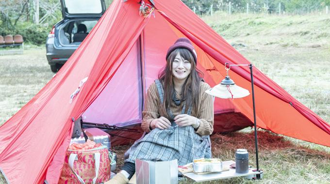 平地にテントやキャンプ道具を広げている女性の写真
