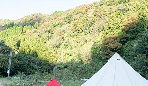木が生い茂る山の中で白と赤のテントの上部分が写っている写真
