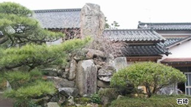 庭の木々の間に、大きな石碑が立っている写真