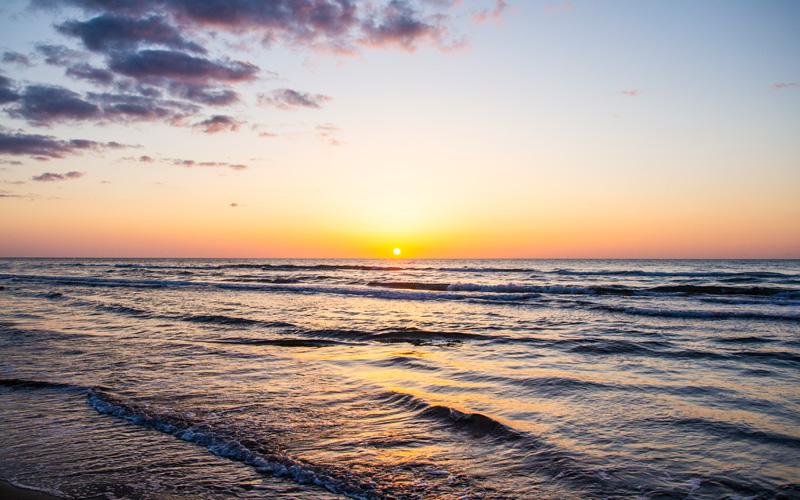 濃紺の海に、オレンジ色の太陽が沈んでいく写真