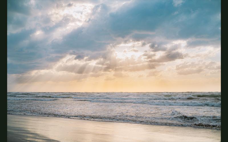 波を打っている海の上で雲の隙間から光が差し込んでいる写真