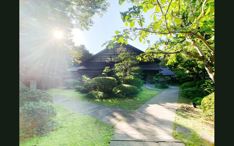 石畳の敷かれた庭に手入れされた草木と木造建築が建っている写真