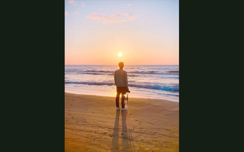 波打ち際でカメラを持って沈む太陽を眺めている写真