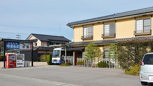 横にバスが停まっている、黄色い和風の建物の写真
