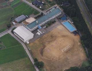 校庭に2000と書かれている宝達小学校の全景を上空から撮影した写真