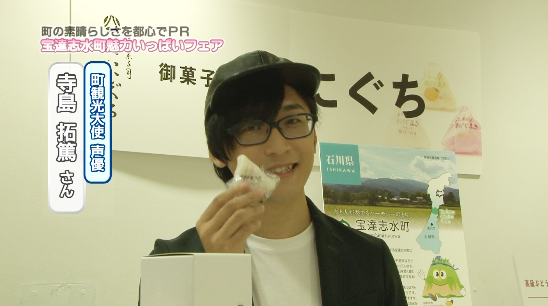 寺島拓篤さんが谷口製菓のおだまきを手に持ってインタビューを受けている写真