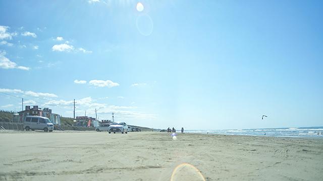 青空の下、浜辺に何台もの車が停まっている写真
