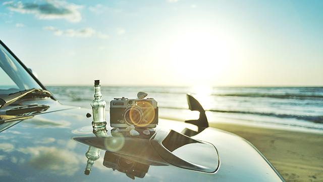 海を背景に車のボンネットの上にカメラと瓶が置かれている写真