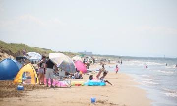 波打ち際の砂浜にパラソルやテントが設置され人々が遊んでいる写真