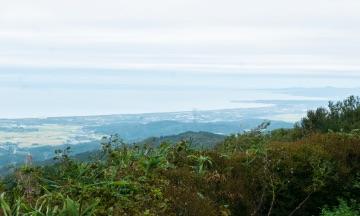 山頂から、緑の山脈と平野と海とを一望した風景の写真