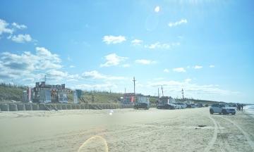 青空の下、砂浜の上に屋台と乗用車が並んでいる写真