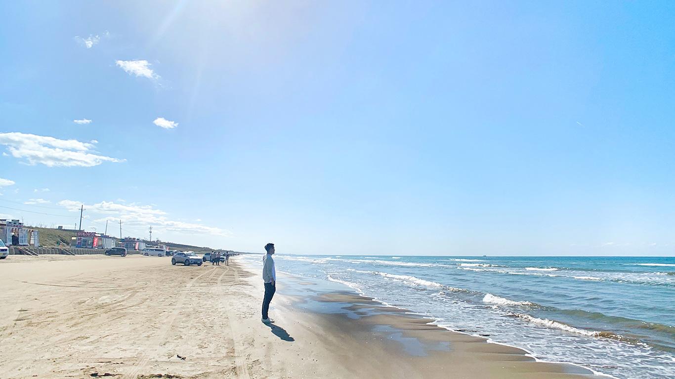 海岸の波打ち際に立ち海を見つめている男性の写真