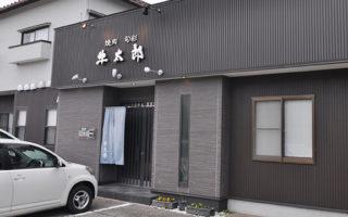黒い壁の建物に店名の牛太郎が飾られ、駐車場に車が止まっている写真