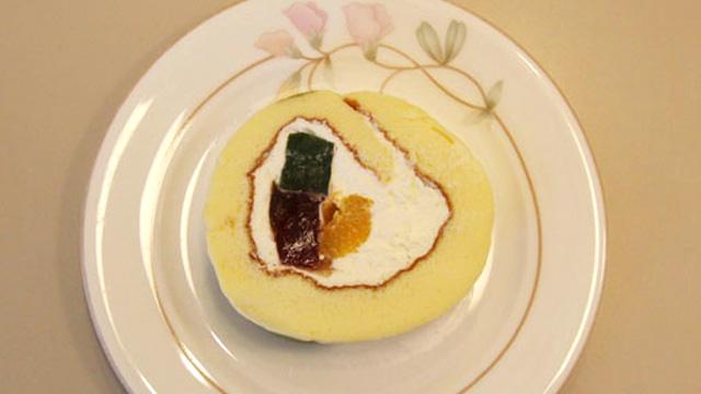 茶色、緑色、オレンジ色の食材をクリームで包んだロールケーキを真上から撮影した写真