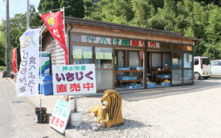 小さいサイズの、果物ののぼりや看板の後ろに平屋の直売所が建っている写真(押水特産直売所のページへリンク)