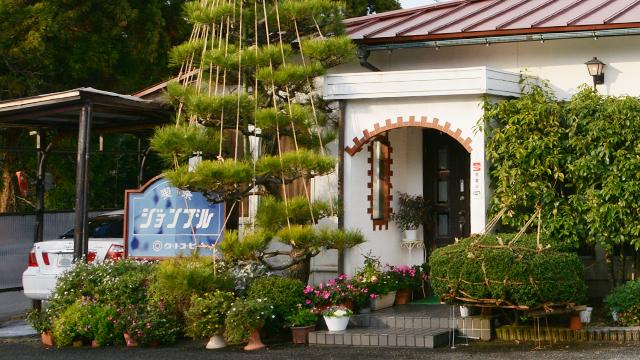 植え込みや鉢植えの花で飾られた、喫茶店の入り口の写真