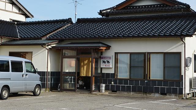 入り口に看板を出している、瓦屋根で壁にタイルを張っている建物の写真