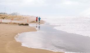 波がひく際の水面の残りに歩いている2人が写っている写真