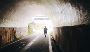 暗いトンネル内から光のさす出口に向かっている人の写真