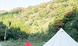 木が生い茂る山の中で白と赤のテントの上部分が写っている写真(宝達志水町のサイト 所司原キャンプ場へのリンク)