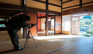 和室内で三脚にセットしたカメラを調整している男性の写真(宝達志水町のサイト 加賀藩十村役 岡部家へのリンク)