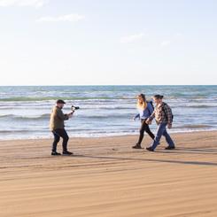海岸の波打ち際で歩いている2人を撮影している人の写真