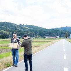 北と書かれた紙を持った人とその撮影者が道路脇に立っている写真