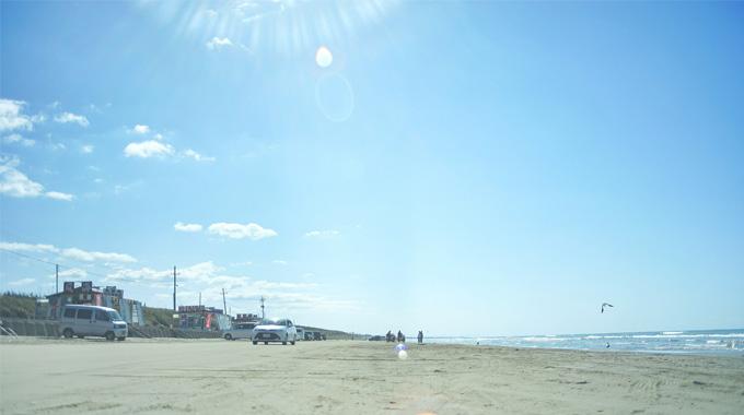 車が走っている砂浜から遠くの風景や波打ち際を写した写真