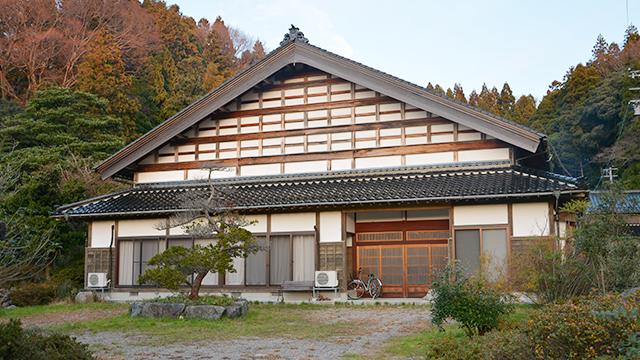 木々を背に、瓦屋根の巨大な建物が建っている写真