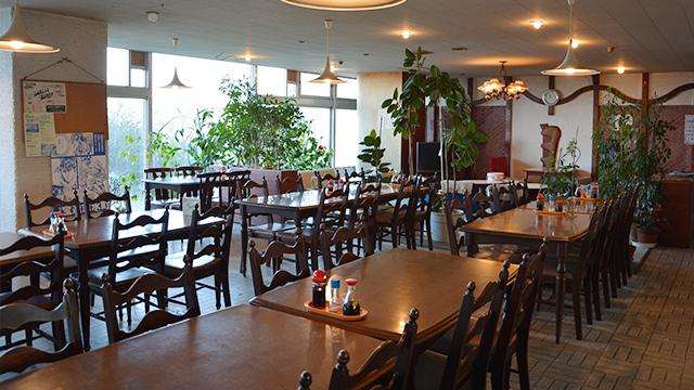 テーブルと椅子が並び、観葉植物が置かれた、レストランの内観の写真