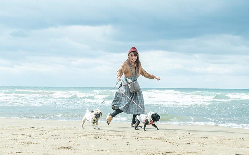 犬を二匹散歩させている女性が、笑顔で浜辺を駆けている写真