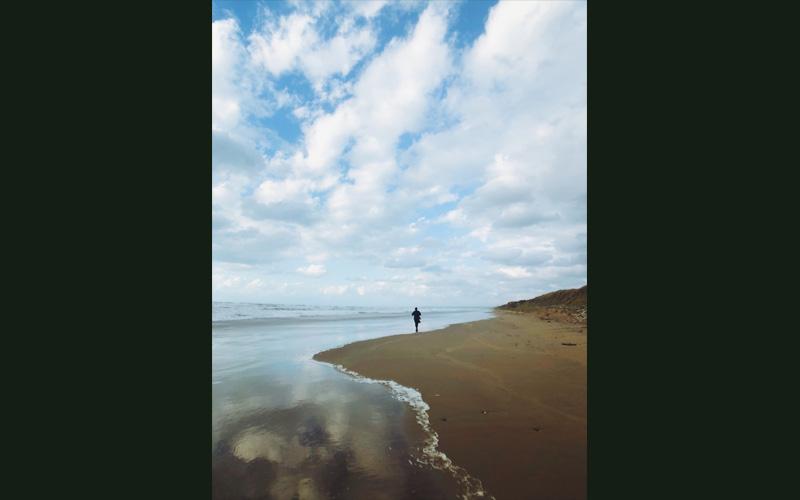 砂浜と波打ち際の境目に立っている人の写真