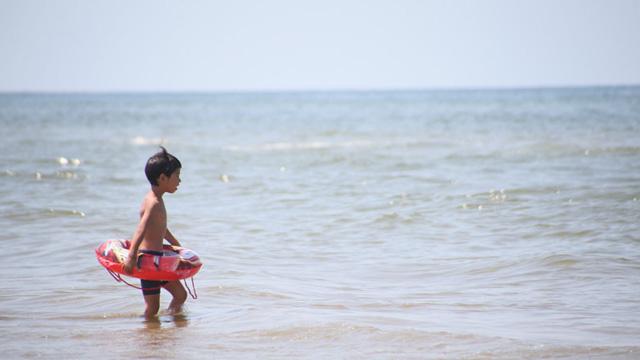 浮き輪を持った男の子が海に入っていく写真