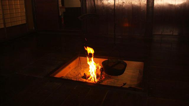 暗い部屋で、囲炉裏の火に鍋があてられている写真
