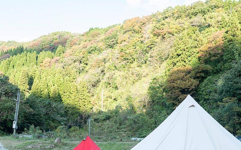 草木が生い茂る山を背景に赤と白のテントの上部が写っている写真