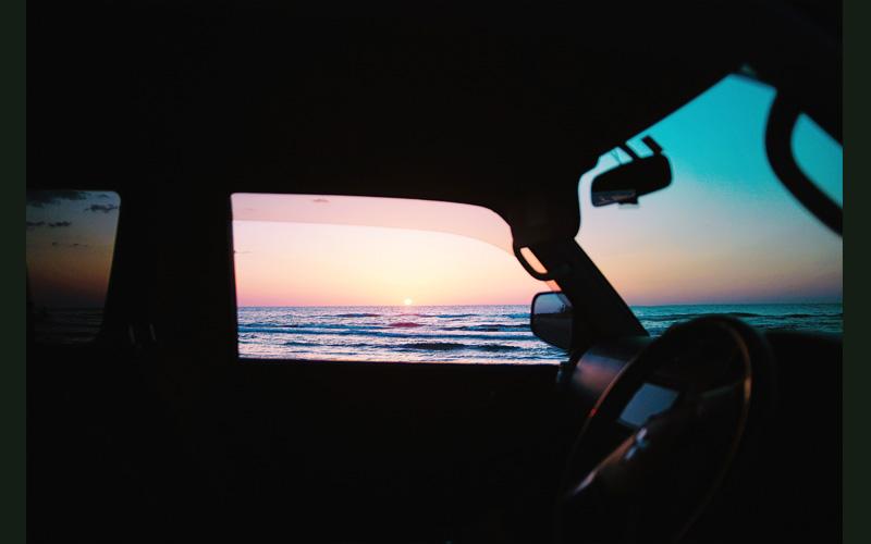 砂浜に止めた車の中から日の沈む海の風景を撮影した写真