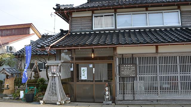 黒い瓦屋根と木の扉がある、そば店の入り口の写真